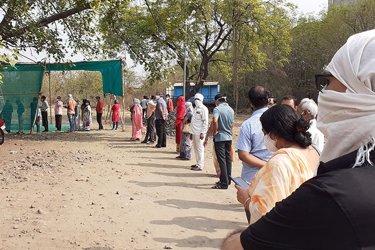 People waiting in line along dusty road for vaccines