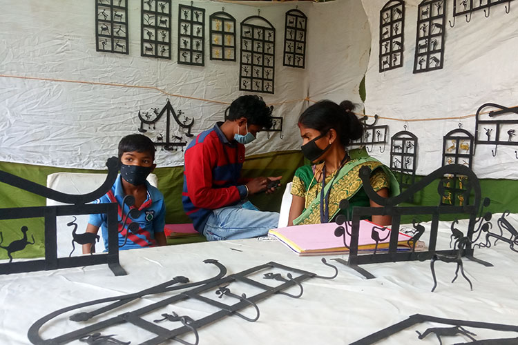 Artisans who make metal wall hangings wait in their shop, without customers